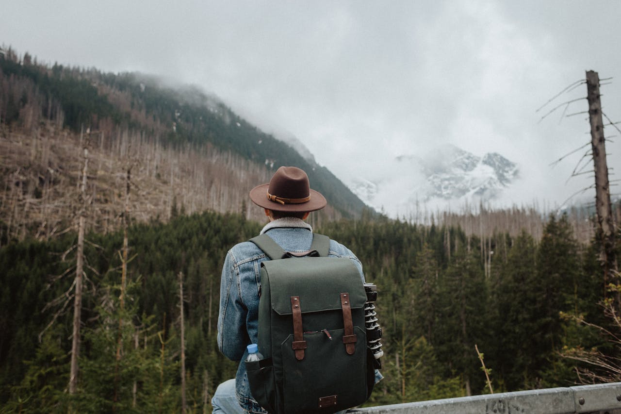 our-mission Back view of a man in a hat and backpack sitting, overlooking a snowy mountain.