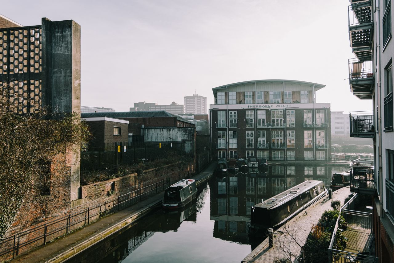 Charming urban canal scene with modern townhouses and barges reflecting in water.